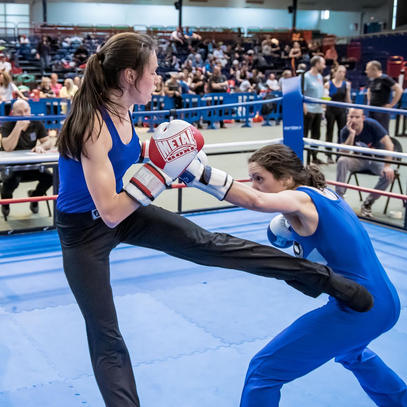 Deux tireuses en assaut sur un ring bleu, l’une lance un coup de pied bas