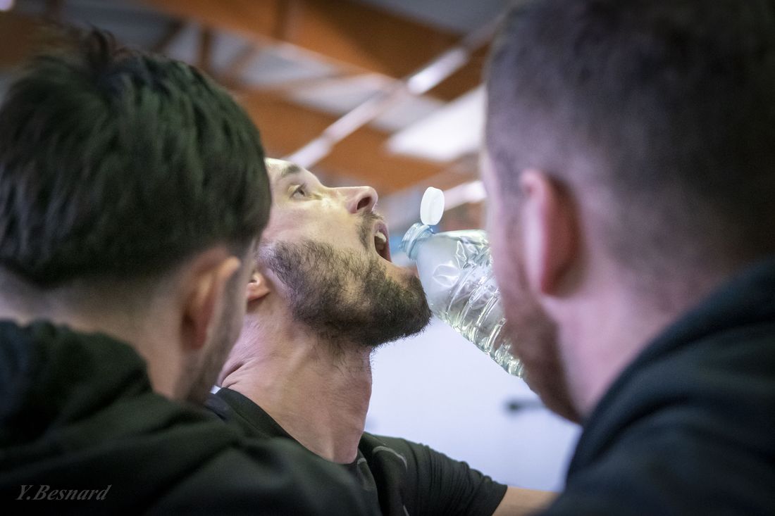 Un tireur boit entre deux reprises, entouré de ses entraîneurs