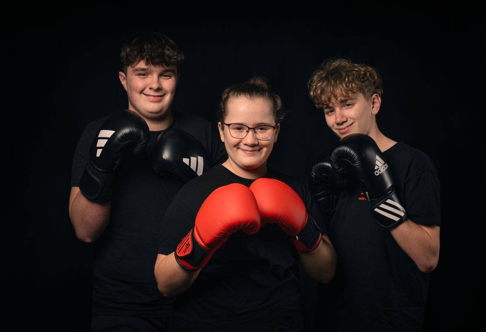 Trois jeunes pratiquants sourient, gants de boxe en garde