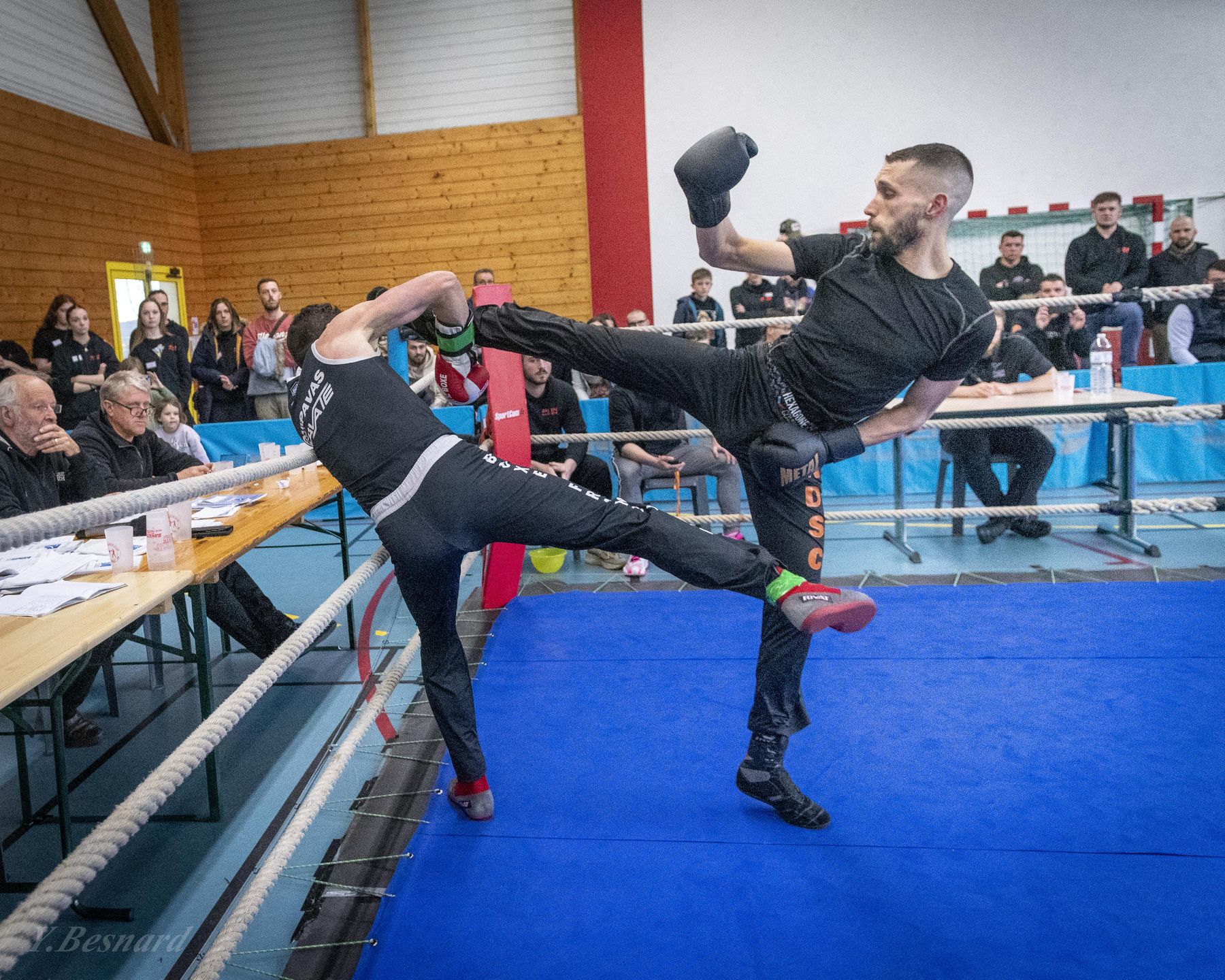 Un tireur saute pour lancer un coup de pied au-dessus de son adversaire qui se baisse, sur un tapis bleu