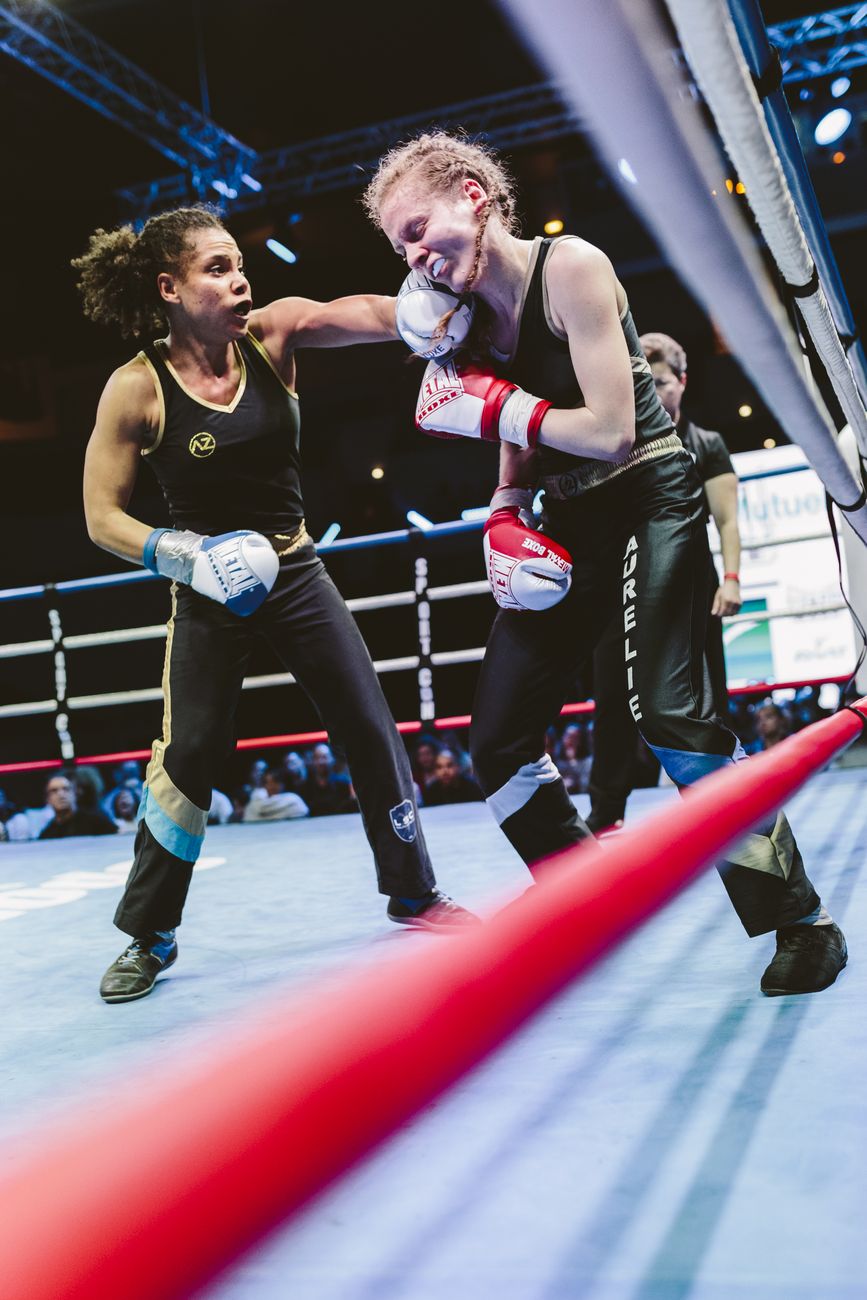 Deux tireuses échangent un coup de poing sur le ring, corde rouge au premier plan